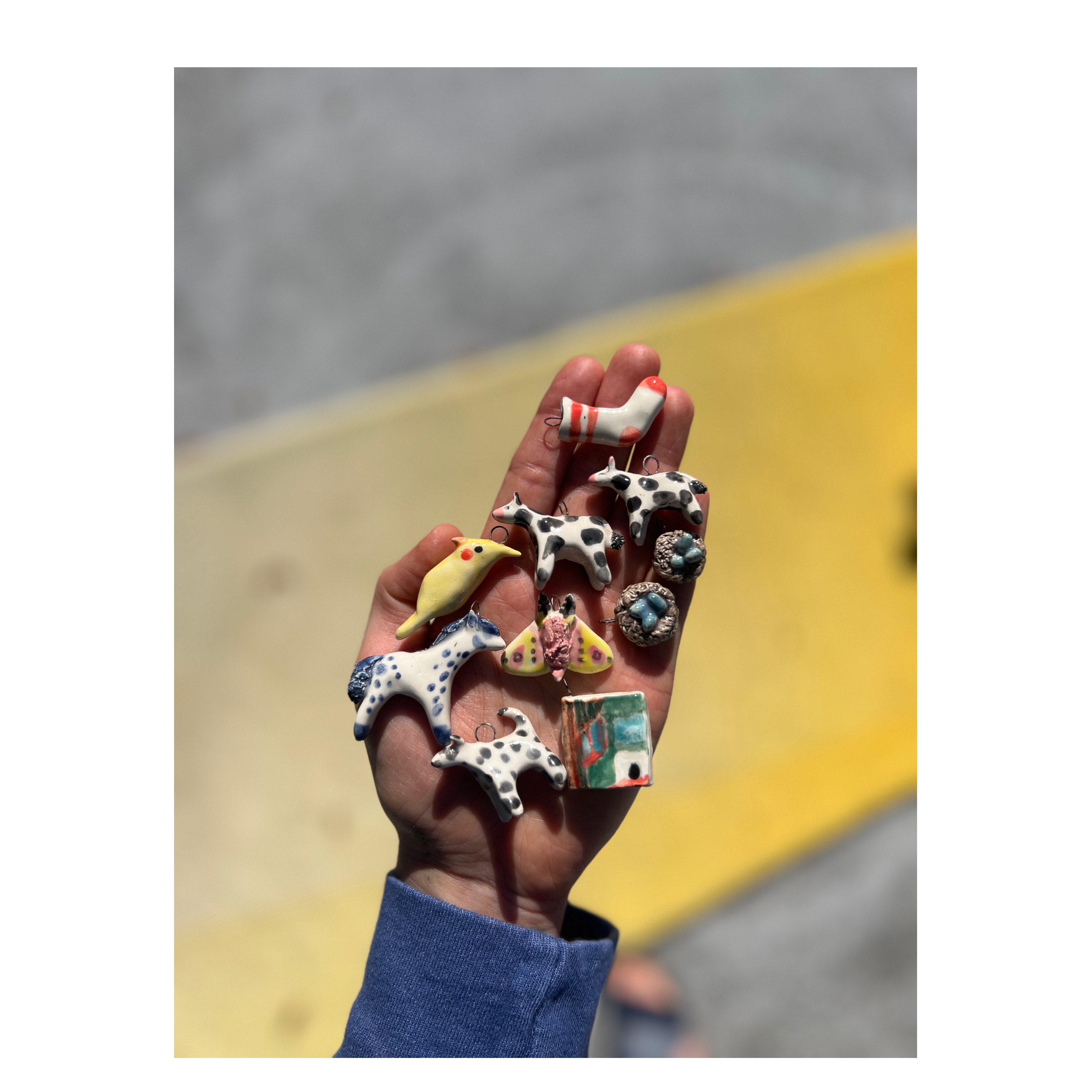 Hand holding 10 small ceramic ornaments in a variety of forms like animals 