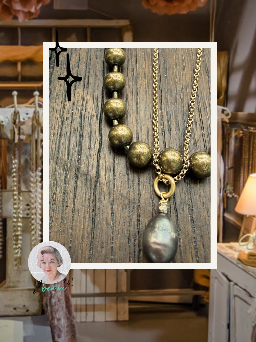 Gold-toned necklace featuring large brushed metal beads and layered chains with a dark teardrop pearl pendant on a rustic wood background.