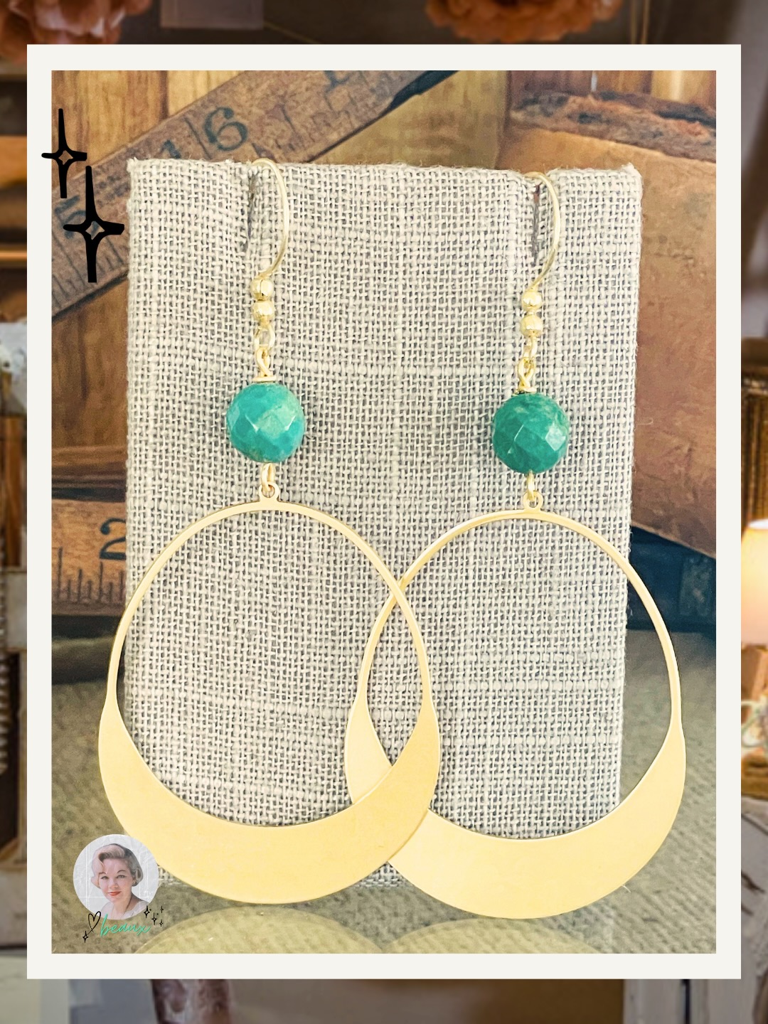 Gold crescent hoop earrings with faceted green gemstone beads, displayed on a textured linen stand.